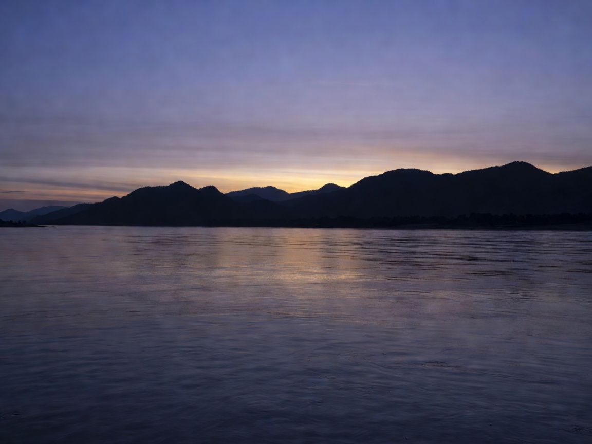 Wide Mekong river at dusk with dark silhouetted hills and a faint glow on the water